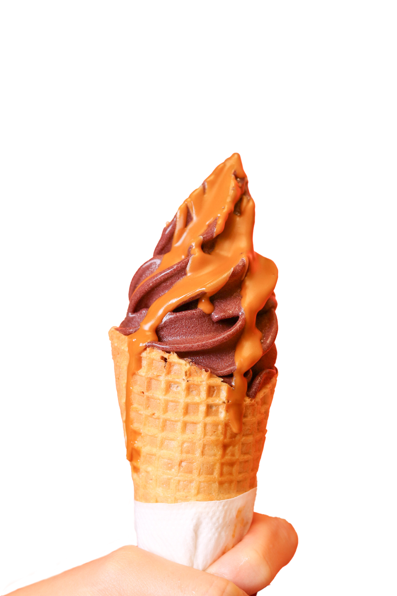 A hand holding a waffle cone filled with swirled açaí soft serve, topped with a generous drizzle of peanut butter sauce. The cone is wrapped with a white napkin.
