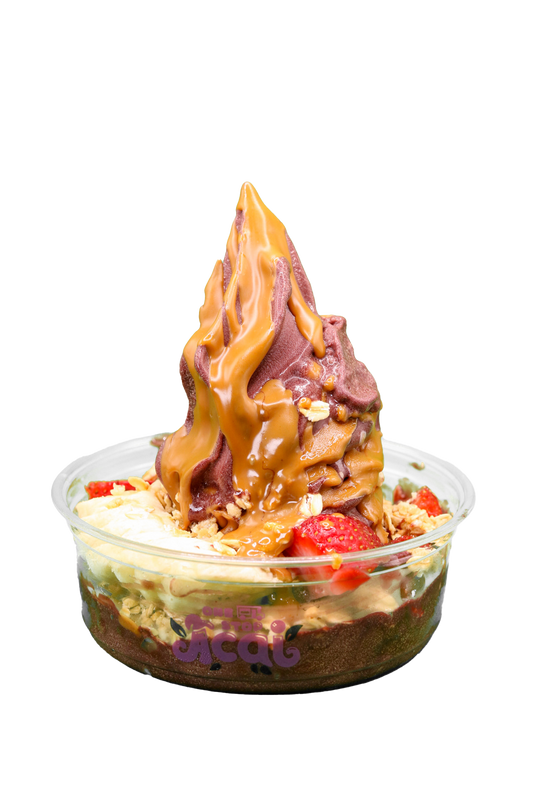 A clear plastic bowl of açaí soft serve topped with a thick peanut butter drizzle, granola, sliced strawberries, banana, and kiwi. The bowl features the 'One Stop Açaí' logo in purple with leaf accents.